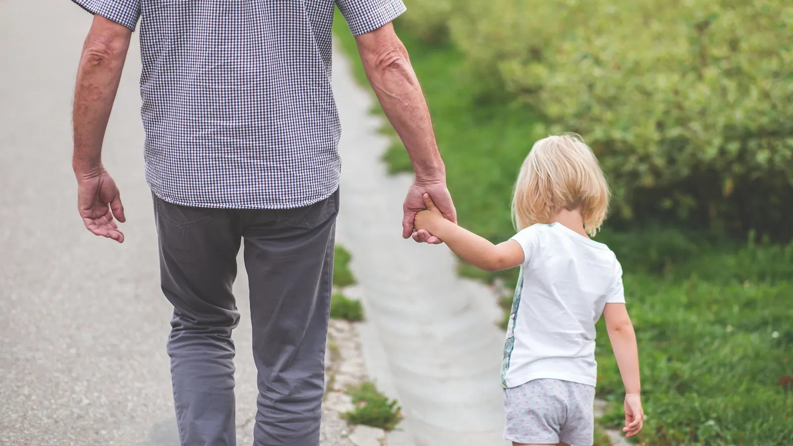 A grandfather and small child walking hand in hand along a path, seen from behind