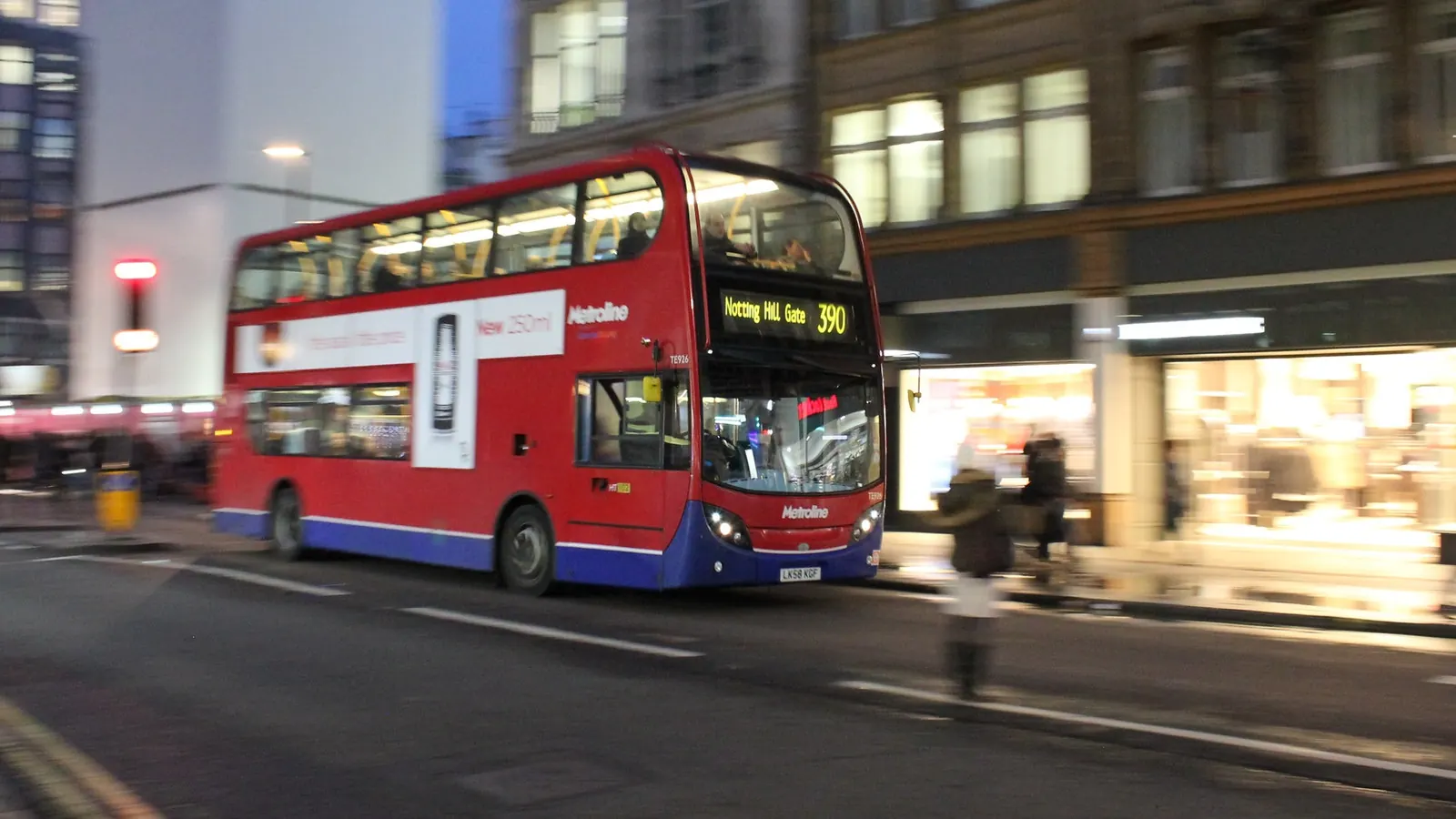 A red double-decker city bus driving along a street