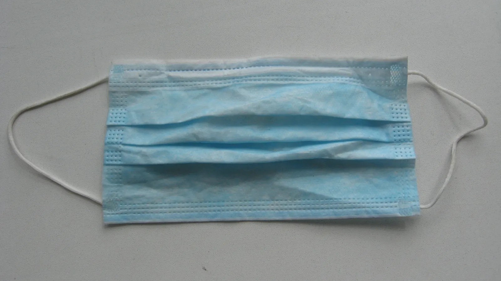 A single blue disposable face mask on a plain grey background