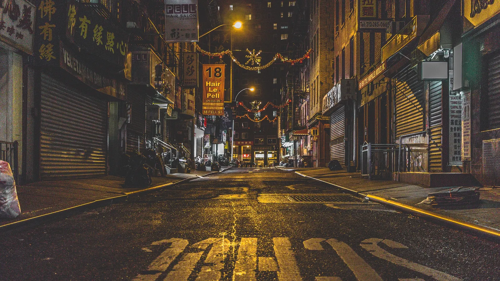 A narrow street in Manhattan’s Chinatown at night, lit by street lamps