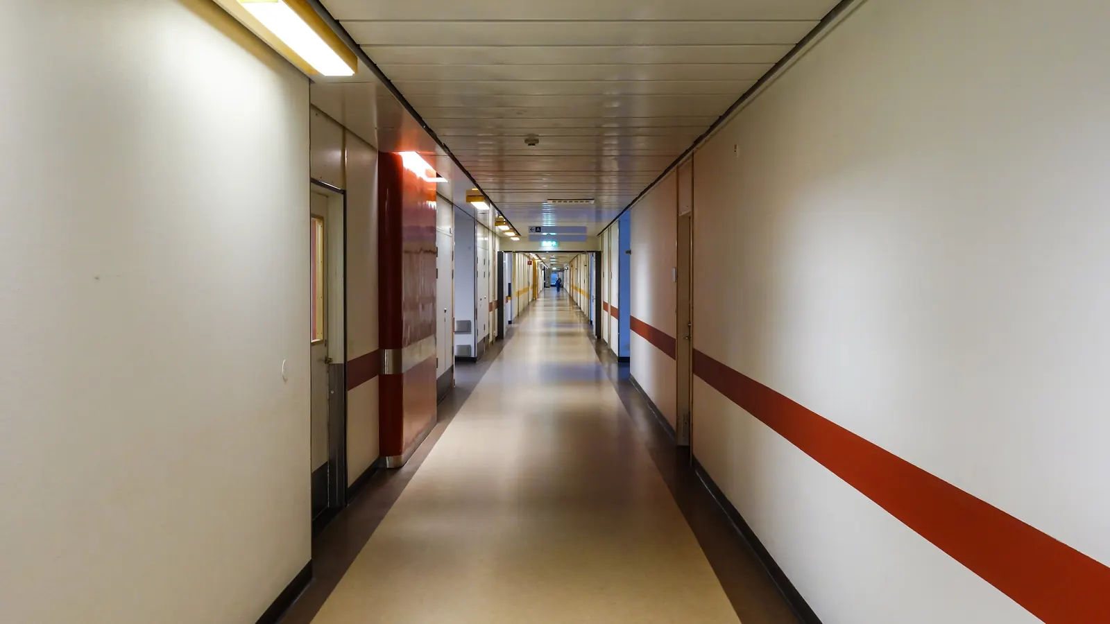 A long, quiet hospital corridor with a red stripe along the wall