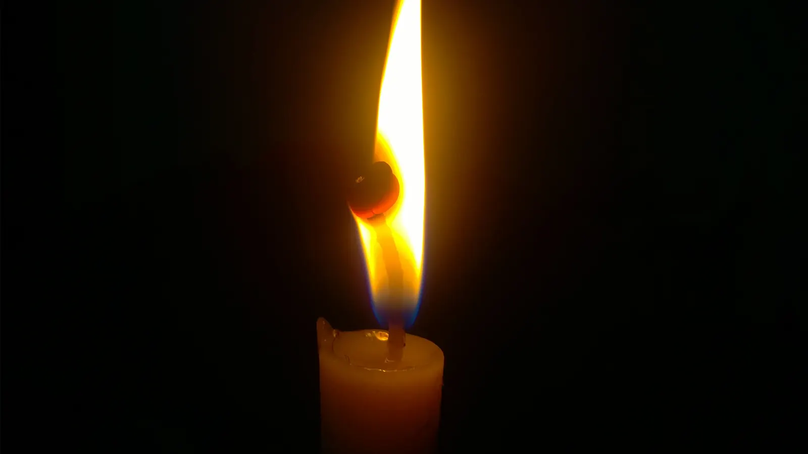 A single candle flame burning against a dark background