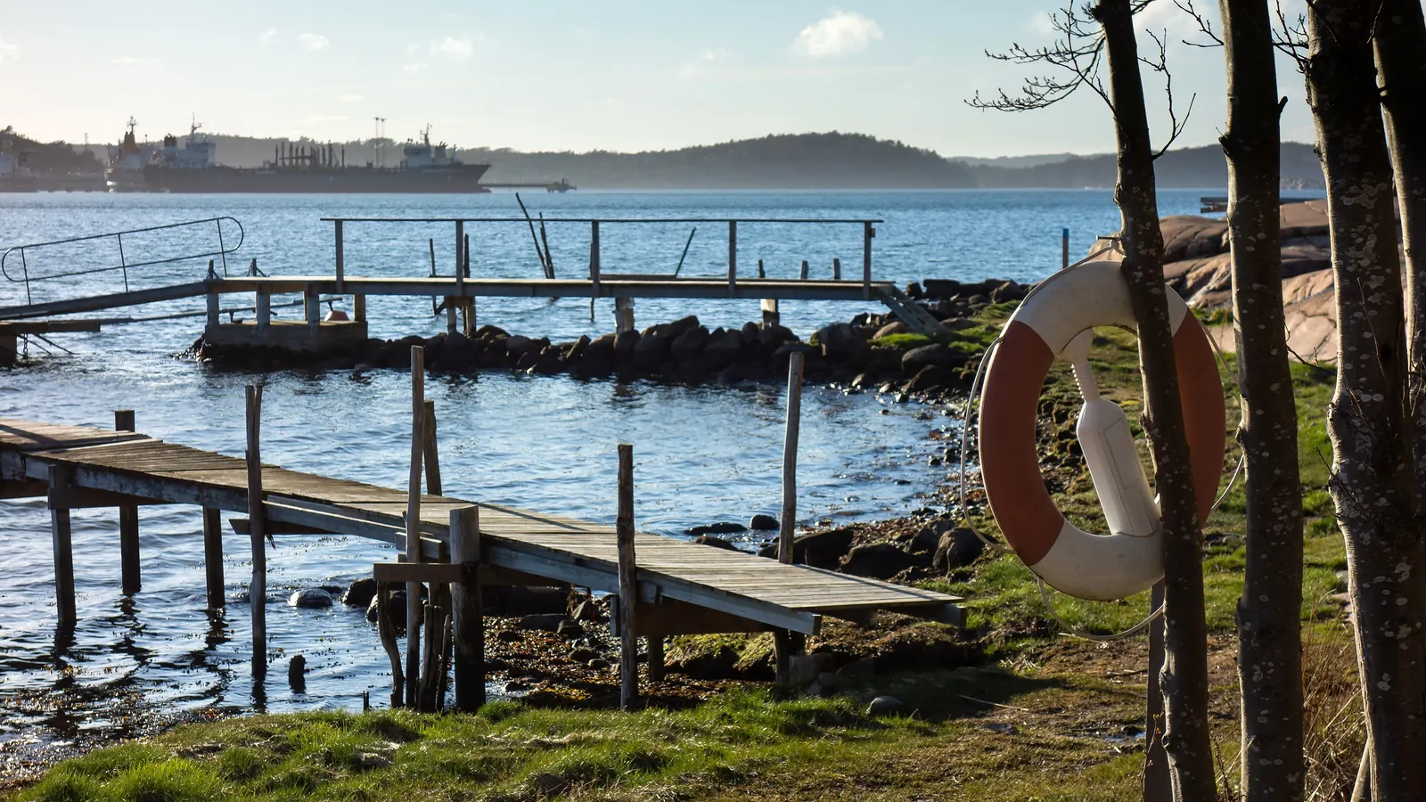 A lifebuoy hanging by a wooden jetty on a calm blue bay