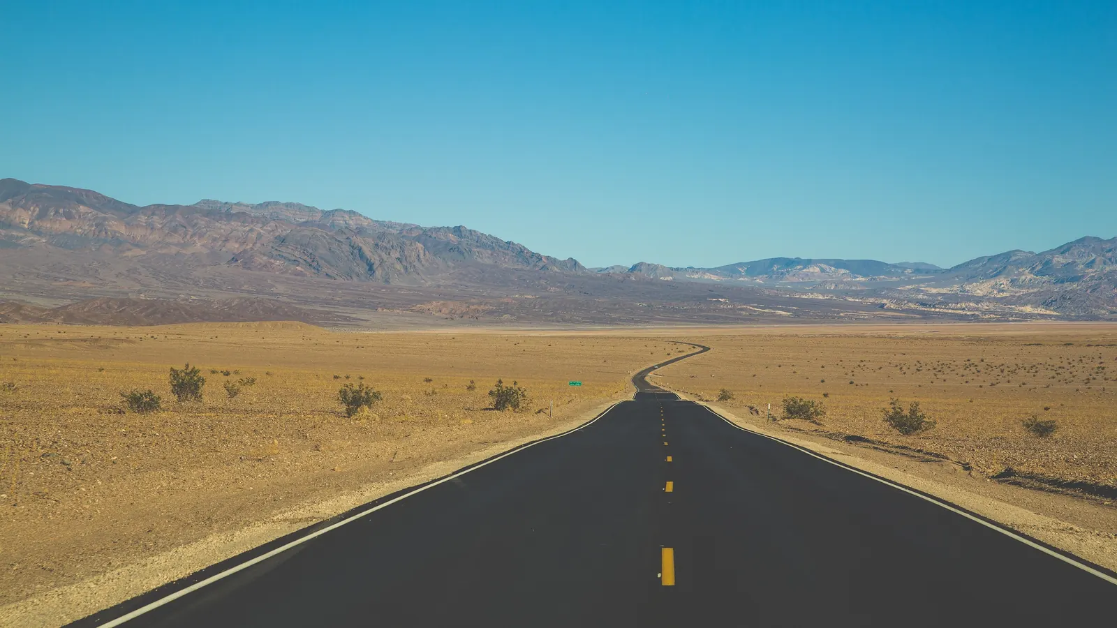 An empty road winding across a desert valley toward distant mountains