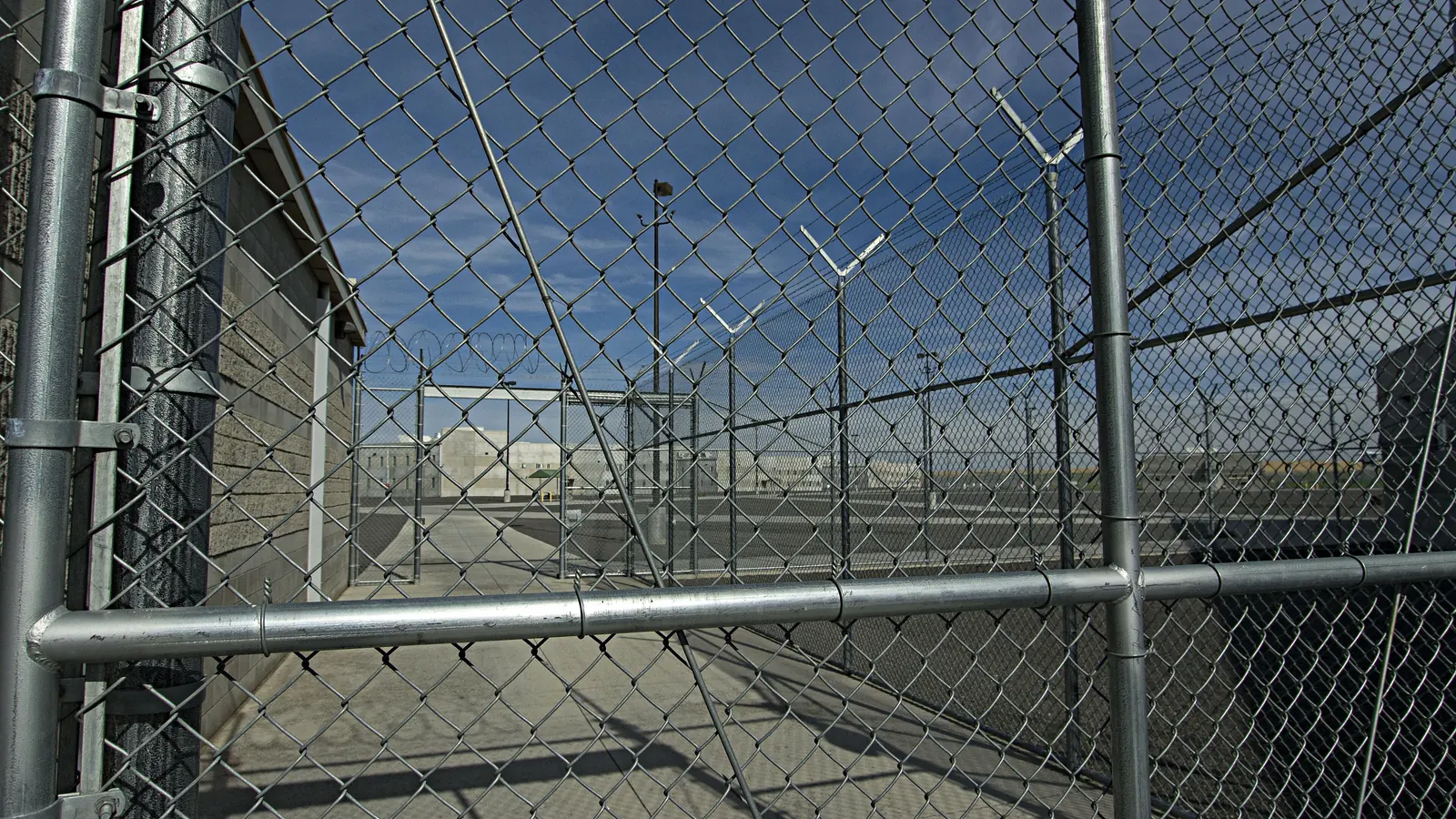 Chain-link fencing topped with wire around a prison yard under a blue sky